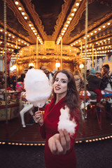 Portrait of a beautiful young girl with white cotton candy in front of a carousel horse
