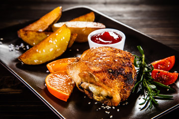 Barbecue chicken thighs with baked potatoes on wooden background