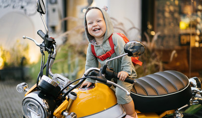 Fototapeta na wymiar Small happy baby in a bodysuit sits on a motorcycle and experiences an emotion of joy. Motorcycle advertising.