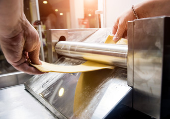 Chef rolling dough with a pasta machine. Pasta maker machine. Homemade italian style cuisine. Restaurant.