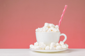 A coffee Cup with a saucer filled with marshmallows and a red tube on a red background.