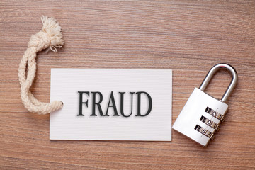 Combination number padlock on wood background with fraud written on label tag