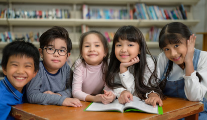 A Group of Asian Kids Reading Book in School Library with a Shelf of Book in Background, Asian Kid Education Concept