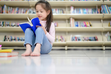 Asian Kid Student Girl Reading Book and Siiting on Floor in School Library with shelf of book in background, Asian Kid Education Concept