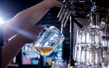 Bartender pouring draft beer at glasses in the bar. Restaurant.