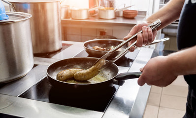 Chef cooks fried potatoes with pieces of meat in a restaurant kitchen