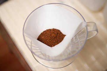 Drip brewing; clear glass of coffee mug and paper dripping bag with ground coffee in soft sunlight at home.