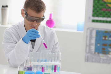 Fototapeta premium A male chemist holds test tube of glass in his hand overflows a liquid solution of potassium permanganate conducts an analysis reaction takes various versions of reagents using chemical manufacturing.