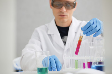 Fototapeta premium A male chemist holds test tube of glass in his hand overflows a liquid solution of potassium permanganate conducts an analysis reaction takes various versions of reagents using chemical manufacturing.