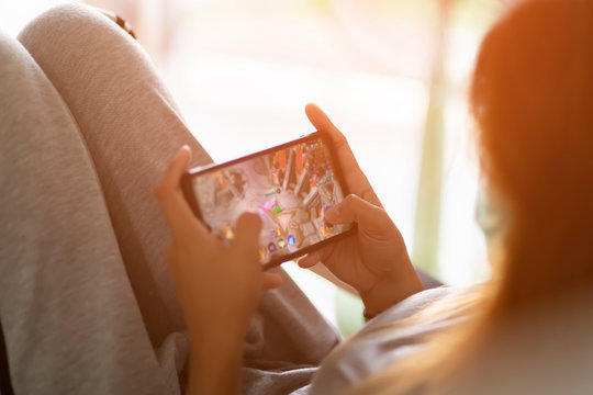 Asian girl are playing the mobile game with blurred on screen at home. The hand is touch screen for play game in the smartphone.