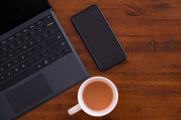 Laptop keyboard with smartphone and a cup of coffee/tea on a rustic wooden table. Modern Office...