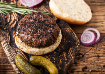 Fresh grilled minced pepper beef burger on vintage chopping board with buns onion and tomatoes on wooden background. Top view