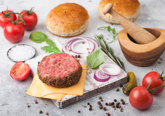 Fototapeta na wymiar Fresh raw minced pepper beef burger on vintage chopping board with buns onion and tomatoes on wooden background.Mortar with pestle with pickles and basil.