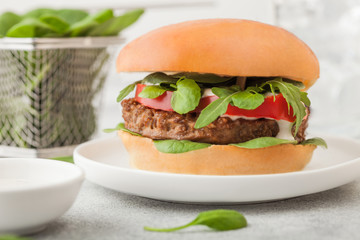 Healthy vegetarian meat free burger on round ceramic plate with vegetables and spinach on light table background.