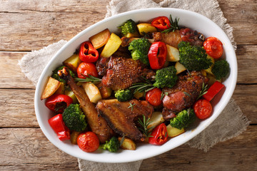 Balsamic chicken with potatoes, broccoli, tomatoes and bell pepper close-up in a baking dish. Horizontal top view