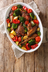 Baked homemade chicken with seasonal vegetables and herbs close-up in a baking dish. Vertical top view