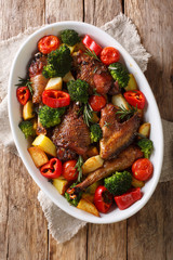 Fried pieces of chicken with vegetables and herbs close-up in a baking dish. Vertical top view