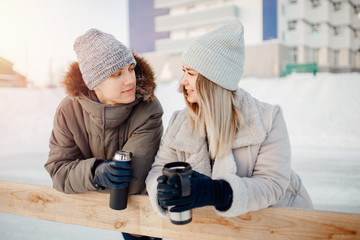 Loving couple drinks hot tea or coffee from thermos mugs on winter street in ice rink