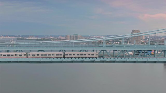 Aerial: Metro train crossing the Ben Franklin Bridge and Delaware River at sunset. In the background is the city skyline. Philadelphia, USA
