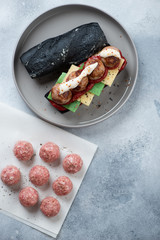 Sub with meatballs and black baguette on a grey plate, flatlay over light-blue stone background, vertical shot