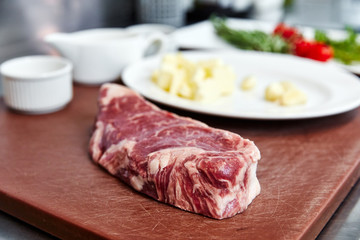 raw piece of meat lies on the board, prepares for cooking, against the background of vegetables