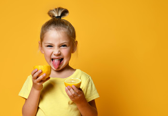 Little smiling cute girl in yellow t-shirt holding halves of fresh sour ripe lemon fruit and...