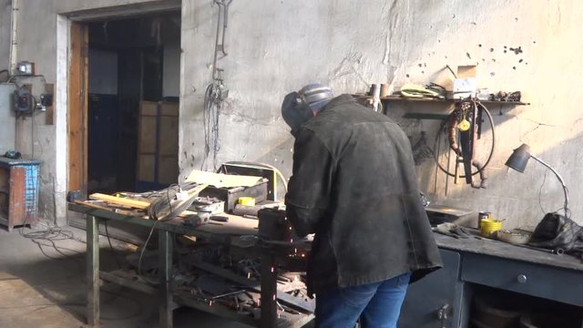 A male welder at work. A masked man is welding metal parts