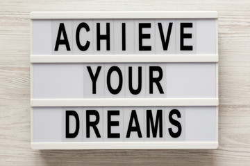 'Achieve your dreams' words on a lightbox on a white wooden background, top view. Overhead, from above, flat lay.