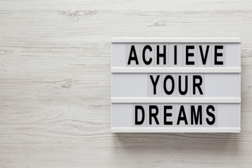 'Achieve your dreams' words on a lightbox on a white wooden surface, top view. Overhead, from above, flat lay. Copy space.