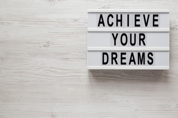 'Achieve your dreams' words on a lightbox on a white wooden background, top view. Overhead, from above, flat lay. Space for text.