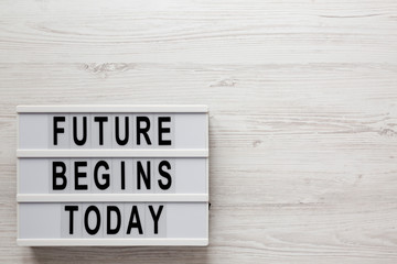 'Future begins today' words on a lightbox on a white wooden surface, top view. Overhead, from...
