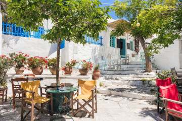 Fototapeta na wymiar Beautiful greek street with flowers and cafe tables in Amorgos island, Greece