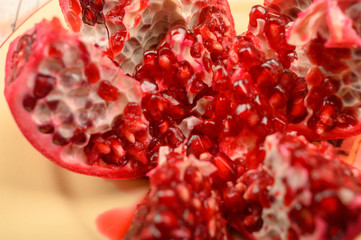 Ripe juicy pomegranate cut into several parts on a ceramic plate on a wooden background. Close up.