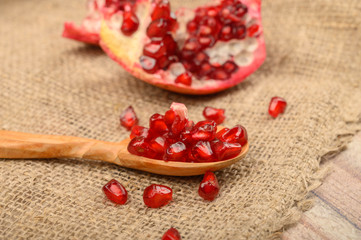 A piece of ripe juicy pomegranate and pomegranate seeds in a wooden spoon on a background of rough homespun fabric. Close up.