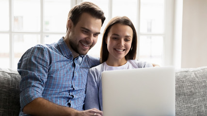 Smiling couple rest on sofa browsing internet on laptop