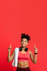 Happy afro sporty girl with towel and earphones pointing up