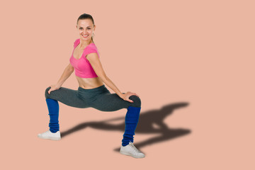 Slim cheerful sporty woman doing wide squat on salmon shade red background