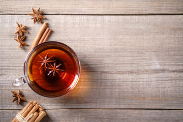 Spiced aromatic black tea. Hot warming beverage in a glass cup with anise and cinnamon on wooden background