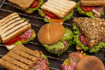 Sandwiches with meat and greens, bun with grains on metal grill. Tasty breakfast. Fast food. Outdoor food concept. .