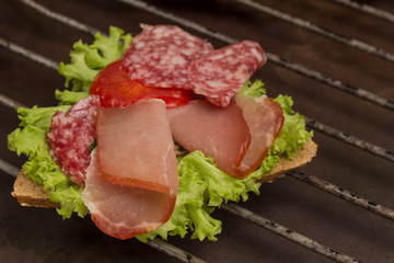 Grilled sandwich with  bacon, salami, cheese and salad on metal grill. Outdoor food concept. .