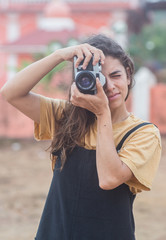 A girl standing outside looking through her camera towards the viewer