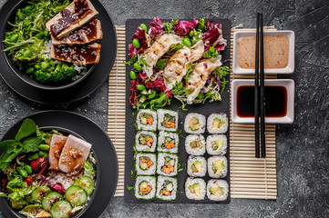 Asian food. Sushi rolls with vegetables, dumplings, salads. Chinese cuisine on a gray concrete background. Top view