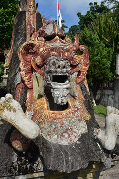 Detail of demon stone statue with weathered surface paint on premises of Tirta Gangga water palace in Bali.