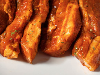 Korean style marinated pork belly slices, close up, on a white plate. Fresh meat preparation.