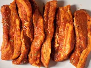 Korean style marinated pork belly slices, close up, on a white plate. Fresh meat preparation.