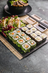 Sushi rolls with vegetables, dumplings, salads. Chinese cuisine on a gray concrete background. Asian food. Vertical shot