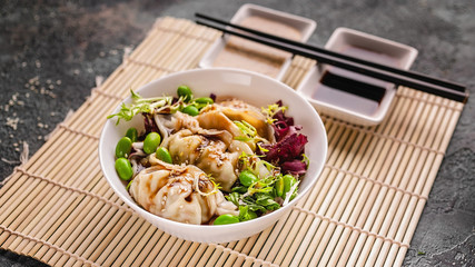 Close up dumplings and salad with green beans on a bamboo mat. Chinese cuisine on a gray concrete background. Asian food.