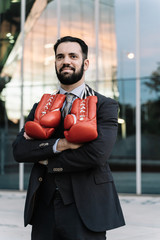 Businessman smiling with sunglasses and red boxing gloves hanging from his neck with his arms...