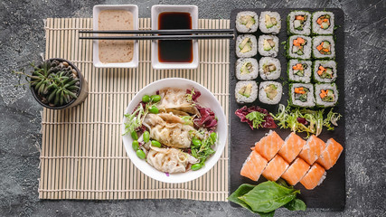 Asian food. Dumplings with green bean salad, rolls with salmon and vegetables on a black stone board. Chinese cuisine. Top view