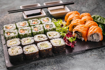 Asian food. Close up rolls with salmon and vegetables on a black stone board. Chinese cuisine. Selective focus